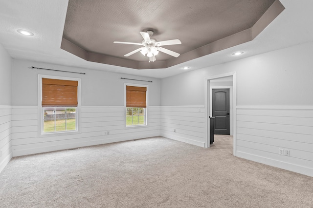 spare room with light carpet, a textured ceiling, a raised ceiling, and ceiling fan