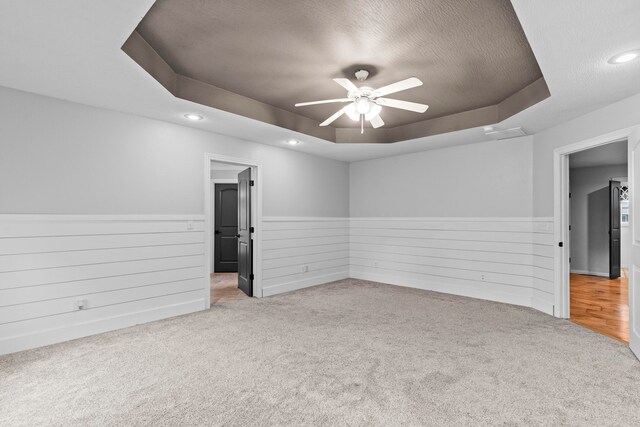 carpeted empty room with ceiling fan, a textured ceiling, and a raised ceiling