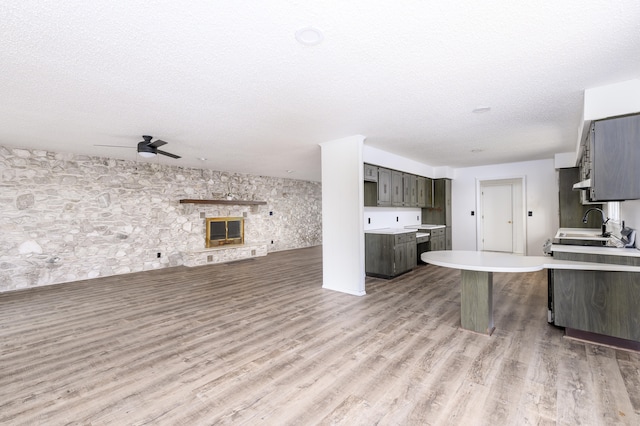 kitchen featuring ceiling fan, kitchen peninsula, a fireplace, light hardwood / wood-style flooring, and a textured ceiling