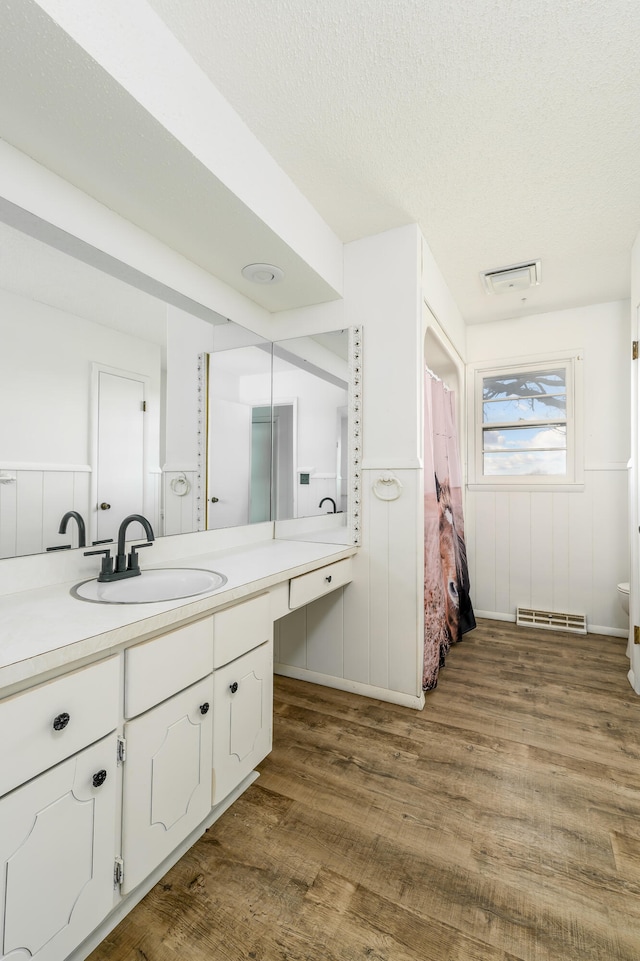 bathroom with wood-type flooring, vanity, toilet, and a textured ceiling