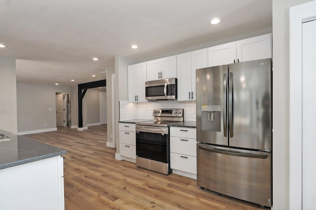 kitchen with stainless steel appliances, light wood-type flooring, tasteful backsplash, and white cabinetry