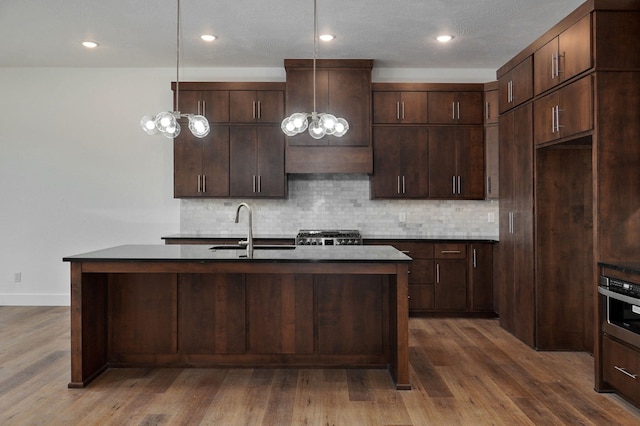 kitchen featuring dark brown cabinetry, hanging light fixtures, sink, hardwood / wood-style floors, and decorative backsplash