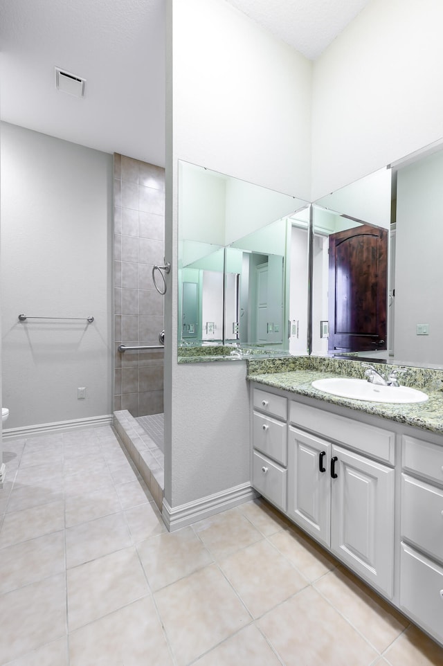 bathroom featuring vanity, tile patterned flooring, a tile shower, and toilet