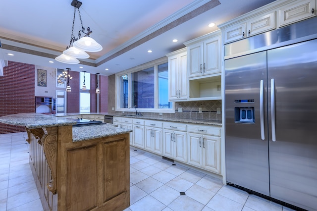 kitchen with pendant lighting, stainless steel built in fridge, ornamental molding, and light stone counters