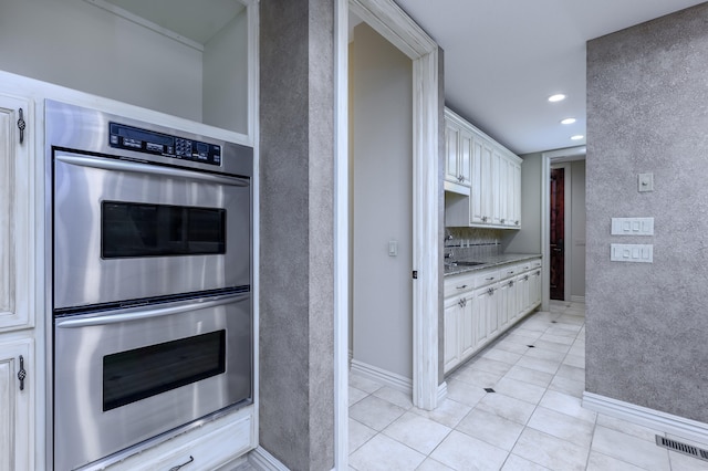 kitchen with light stone counters, stainless steel double oven, light tile patterned floors, and white cabinets