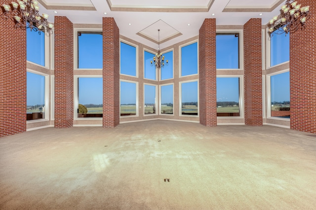 carpeted empty room featuring coffered ceiling, beamed ceiling, a towering ceiling, and a chandelier