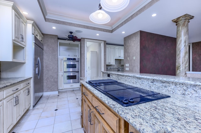 kitchen featuring light stone counters, a raised ceiling, hanging light fixtures, stainless steel appliances, and decorative columns