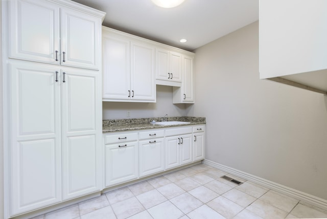 kitchen with light tile patterned flooring, light stone counters, white cabinetry, and sink