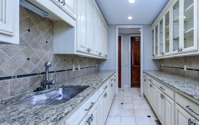 kitchen featuring light stone counters, white cabinetry, sink, and backsplash