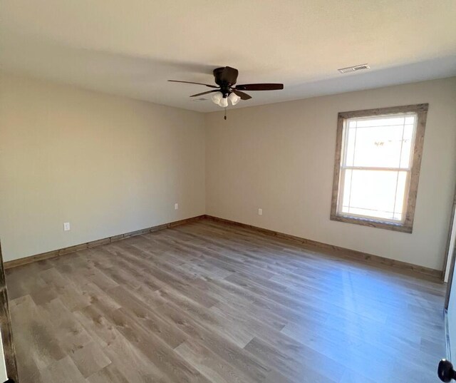 spare room featuring light wood finished floors, visible vents, a ceiling fan, and baseboards