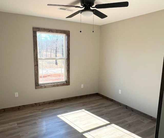 empty room featuring wood finished floors, visible vents, a ceiling fan, and baseboards