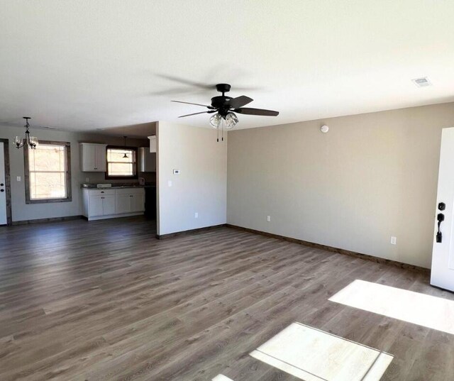 unfurnished living room with baseboards, dark wood-type flooring, visible vents, and ceiling fan with notable chandelier