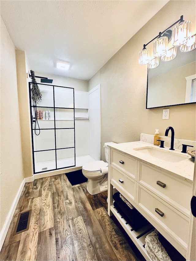 bathroom featuring visible vents, toilet, vanity, wood finished floors, and walk in shower