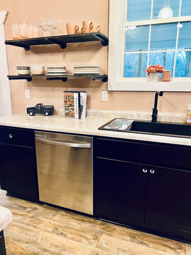 kitchen featuring light countertops, light wood-type flooring, stainless steel dishwasher, open shelves, and a sink