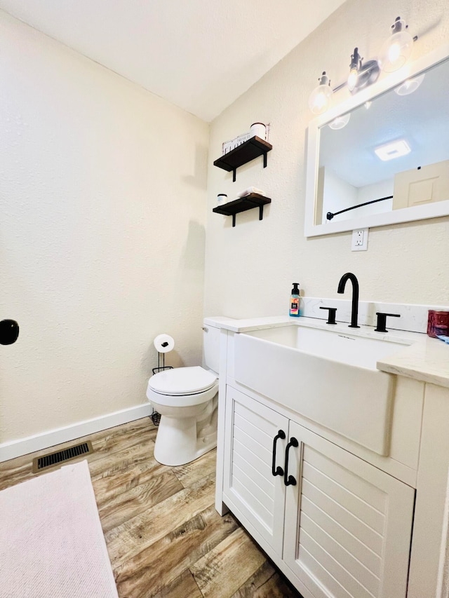 bathroom with baseboards, visible vents, toilet, wood finished floors, and vanity