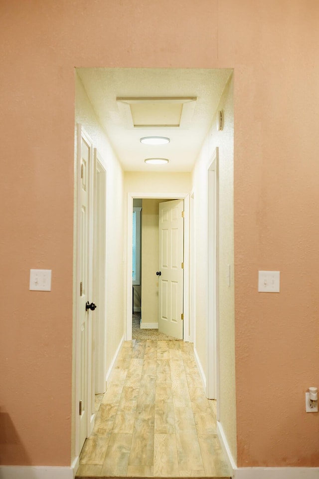 hall with light wood finished floors, attic access, and baseboards