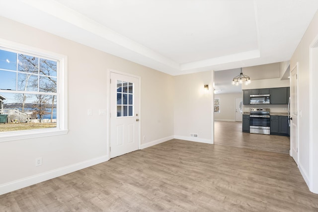 unfurnished living room featuring a wealth of natural light, a chandelier, a tray ceiling, and wood-type flooring