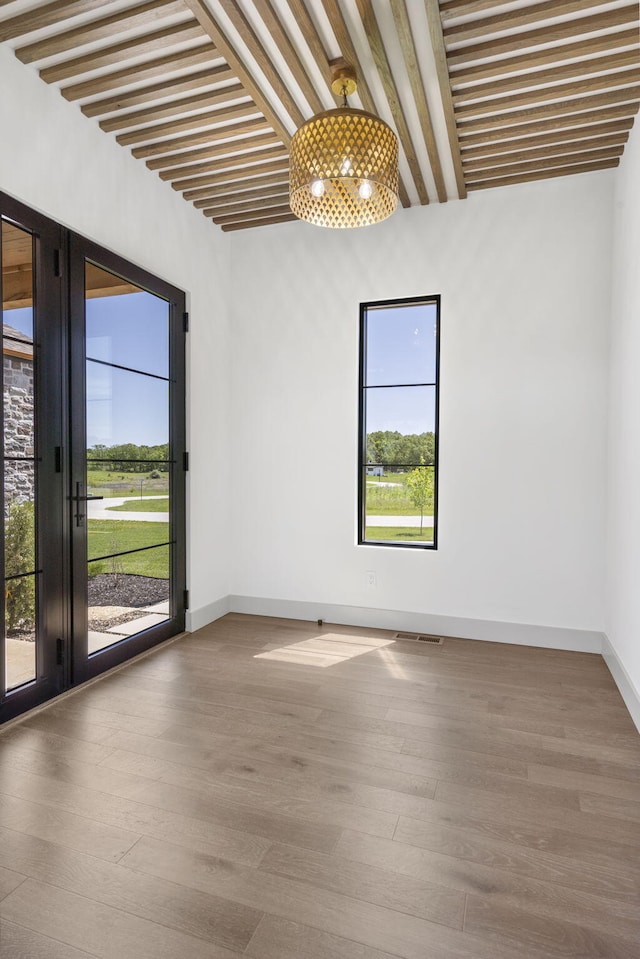 empty room featuring hardwood / wood-style flooring, plenty of natural light, and beamed ceiling