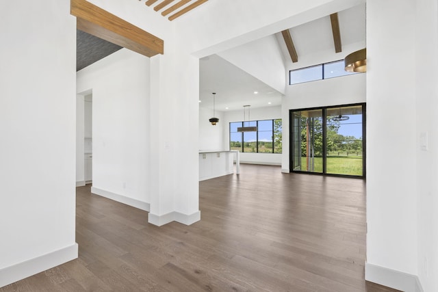 unfurnished living room featuring beam ceiling, a towering ceiling, and wood-type flooring