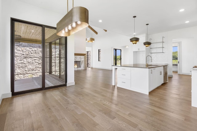 kitchen with light wood-type flooring, sink, white cabinetry, hanging light fixtures, and an island with sink