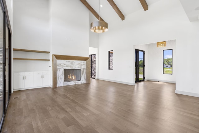 unfurnished living room with a high end fireplace, beam ceiling, light hardwood / wood-style floors, and high vaulted ceiling