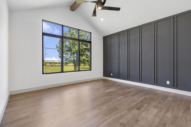 empty room with ceiling fan, light hardwood / wood-style flooring, beamed ceiling, and a healthy amount of sunlight