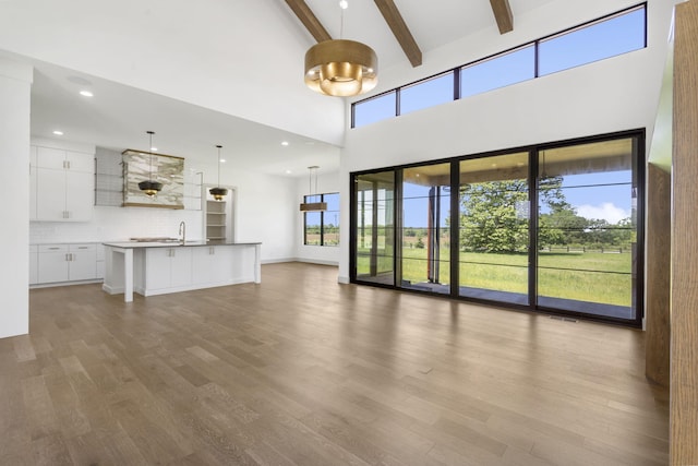 unfurnished living room featuring beam ceiling, a towering ceiling, a healthy amount of sunlight, and hardwood / wood-style flooring