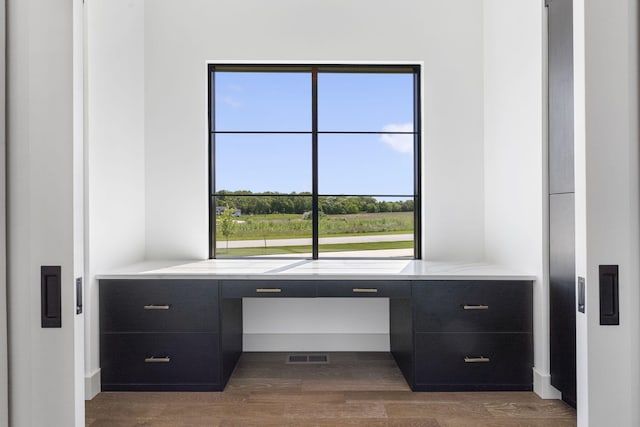 unfurnished office featuring built in desk, a wealth of natural light, and dark wood-type flooring