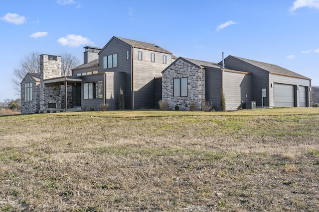 rear view of property featuring central AC unit, a garage, and a yard