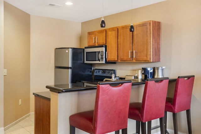 kitchen featuring hanging light fixtures, light tile patterned floors, kitchen peninsula, stainless steel appliances, and a kitchen breakfast bar