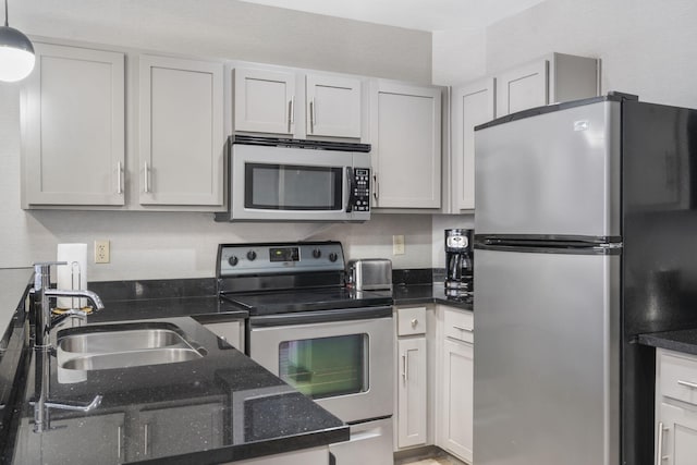 kitchen featuring dark stone countertops, sink, stainless steel appliances, hanging light fixtures, and white cabinetry