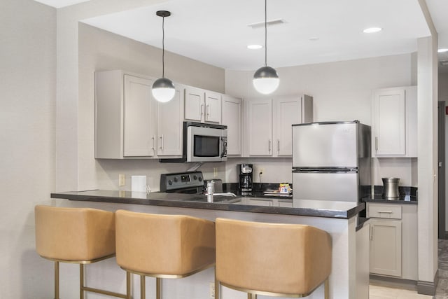 kitchen featuring pendant lighting, appliances with stainless steel finishes, a kitchen bar, and kitchen peninsula