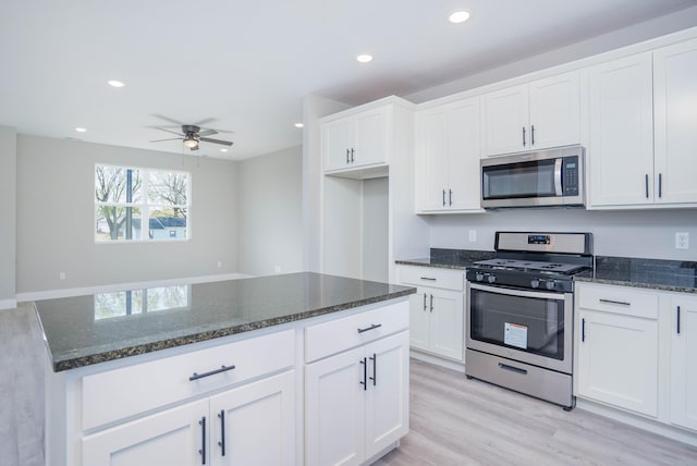 kitchen with white cabinets, appliances with stainless steel finishes, light hardwood / wood-style floors, and dark stone counters