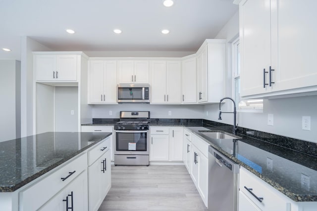 kitchen featuring light hardwood / wood-style floors, dark stone countertops, sink, white cabinets, and appliances with stainless steel finishes