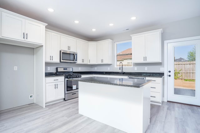 kitchen with a center island, stainless steel appliances, white cabinets, dark stone counters, and light hardwood / wood-style flooring