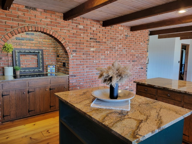 kitchen featuring black electric stovetop, beam ceiling, a center island, light wood-type flooring, and light stone counters