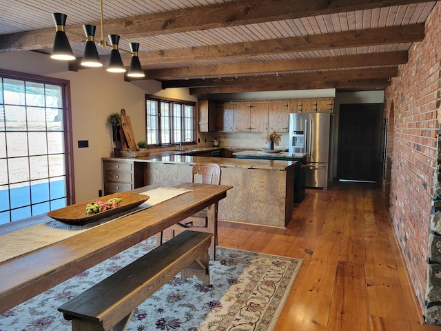 kitchen featuring dark wood-type flooring, brick wall, stainless steel fridge, sink, and pendant lighting