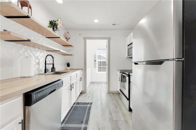 kitchen with white cabinets, sink, butcher block countertops, light hardwood / wood-style flooring, and appliances with stainless steel finishes