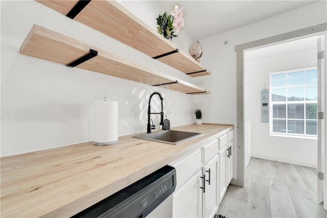 kitchen featuring tasteful backsplash, light hardwood / wood-style flooring, sink, stainless steel dishwasher, and white cabinetry