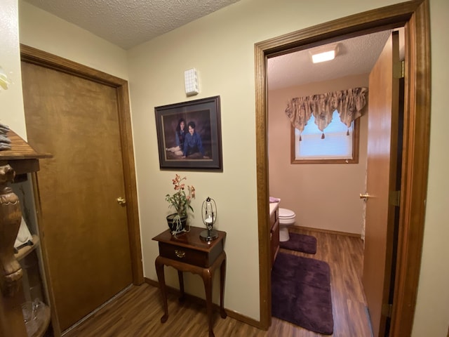 corridor with baseboards, wood finished floors, and a textured ceiling