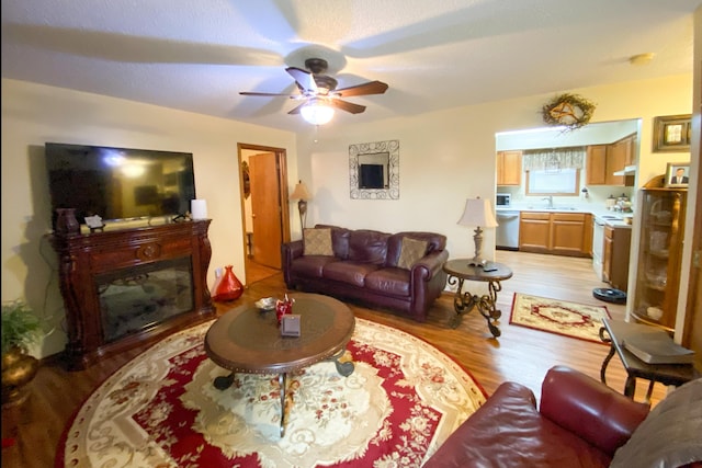 living area featuring light wood-type flooring, a ceiling fan, and a fireplace