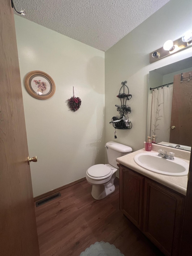 full bathroom featuring wood finished floors, visible vents, toilet, vanity, and a textured ceiling