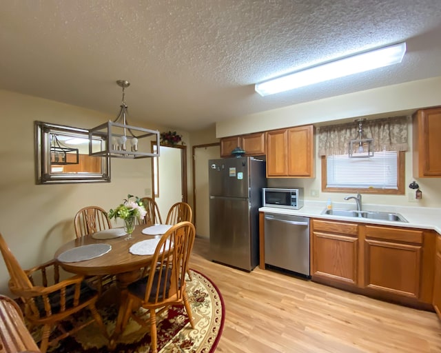 kitchen with a textured ceiling, a sink, brown cabinetry, stainless steel appliances, and light wood finished floors