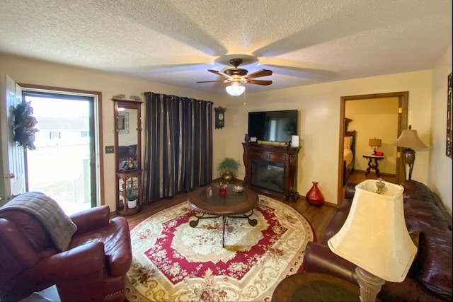 living room with wood finished floors, a ceiling fan, a glass covered fireplace, and a textured ceiling
