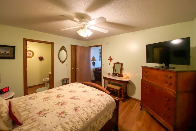 bedroom featuring light wood-style flooring, a textured ceiling, ensuite bathroom, baseboards, and a ceiling fan
