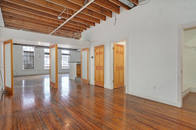 unfurnished living room with a towering ceiling, wood-type flooring, and beamed ceiling