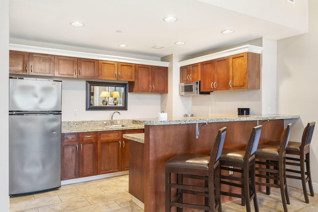 kitchen with light stone counters, sink, kitchen peninsula, stainless steel appliances, and a breakfast bar