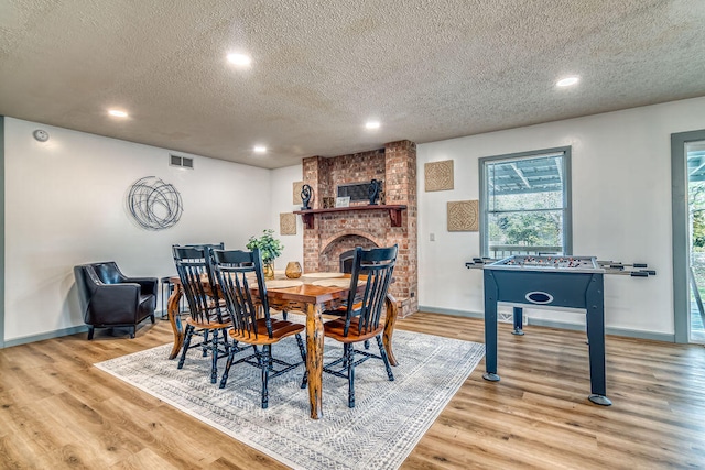 dining room featuring a textured ceiling, a fireplace, and light hardwood / wood-style flooring