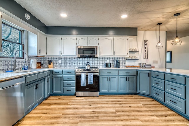 kitchen with white cabinets, pendant lighting, sink, light hardwood / wood-style flooring, and stainless steel appliances