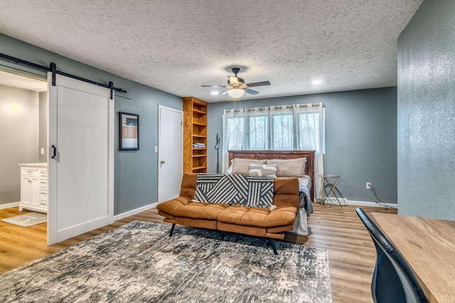 bedroom with light wood-type flooring, ensuite bath, ceiling fan, and a barn door